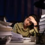 woman looking for ways to prevent burnout at work sitting at a desk stacked high with books and papers